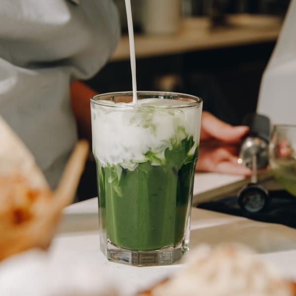 Milk being poured into a glass of vibrant green matcha, creating a swirling pattern.