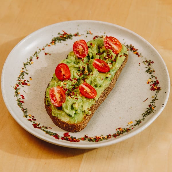 Avocado toast with cherry tomatoes and chili flakes on a white plate with herb garnish.