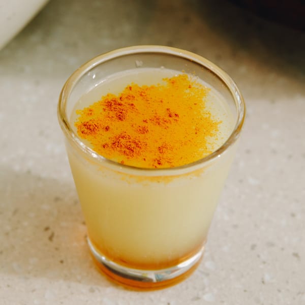A light yellow drink in a clear glass, topped with a vibrant orange powder.