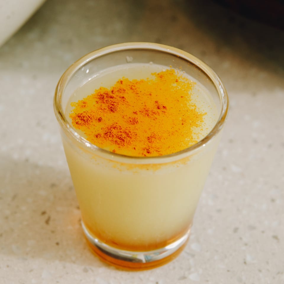 A light yellow drink in a clear glass, topped with a vibrant orange powder.